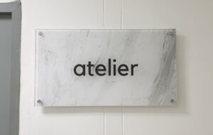 Marble-pattern acrylic wall sign with minimalist branding mounted using stainless steel standoffs.